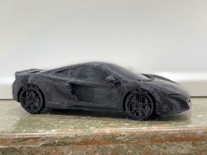 A black, 3-D printed McLaren racecar sits on a marbled countertop.